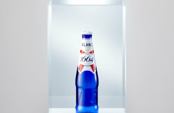 Kronenbourg Blanc bottle placed under a glass display case, simulating a museum exhibit.