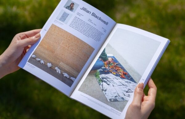 Hands holding the open Cranbrook 2024 Graduate Catalog outdoors